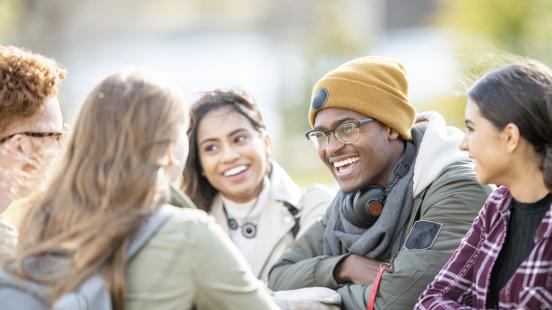 Étudiantes et étudiants d'ethnicité mixte souriants en discussion à l'extérieur.