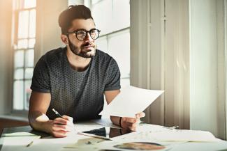 Homme assis pensif regardant au loin tenant un papier et un crayon dans les mains