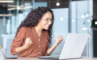 Femme hispanique heureuse devant un portable les poings fermés symbolisant une bonne nouvelle