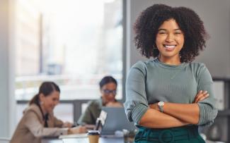 Femme croisant les bras et souriant et collègues en réunion à l'arrière-plan