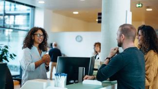 Femme souriante qui accueille deux personnes à son bureau