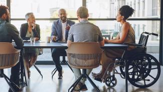 Cinq personnes en réunion, dont une femme en fauteuil roulant, dans un bureau lumineux.
