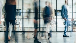 Flou artistique montrant plusieurs personnes marchant dans un couloir d’un bureau moderne à parois vitrées.